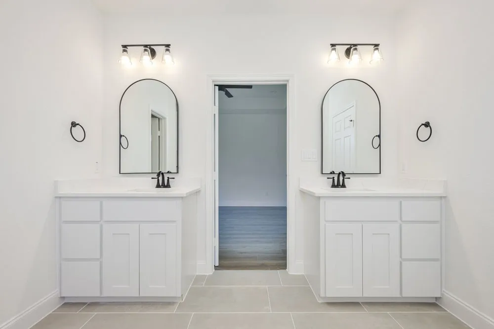Bright primary bathroom with double vanities and arched mirrors